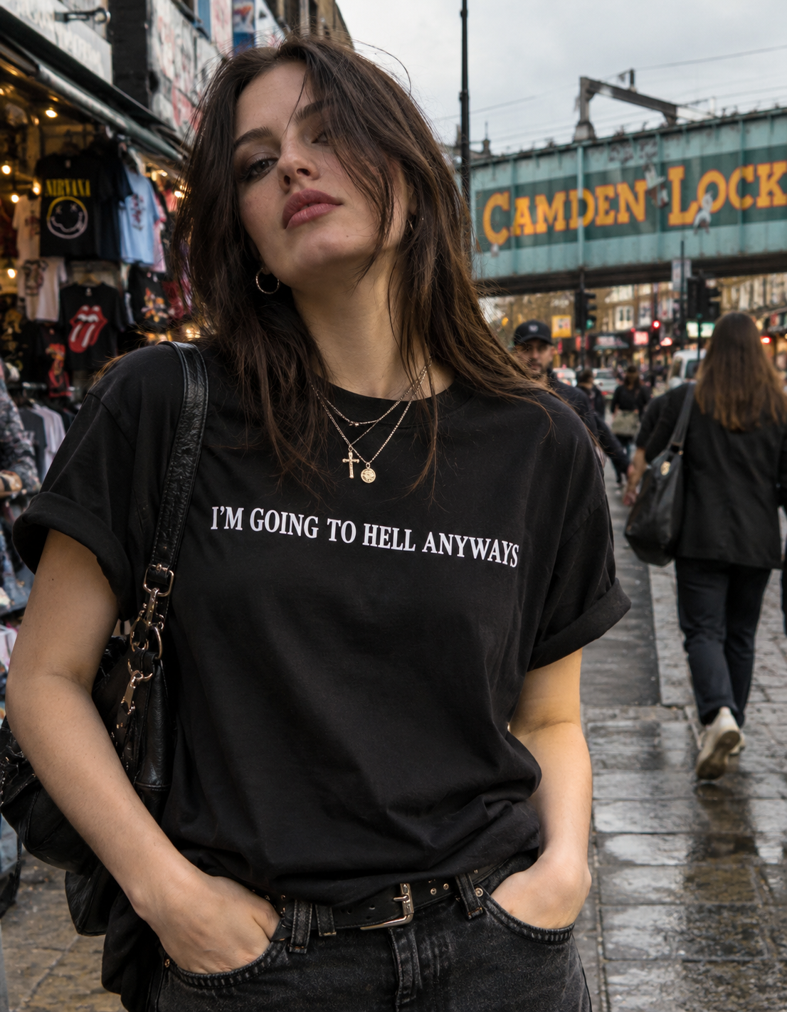 A woman wearing a black graphic t-shirt with the white text 'I'M GOING TO HELL ANYWAYS' stands on a wet city street in front of a Camden Lock background.