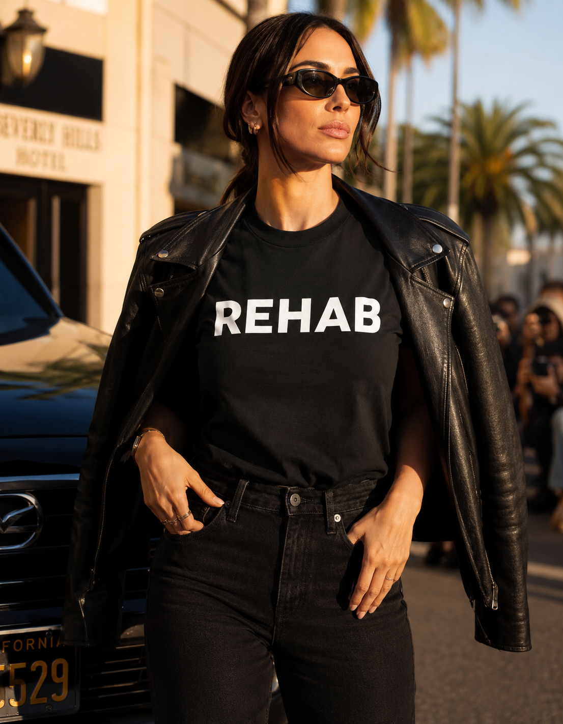 Woman wearing a black t-shirt with 'REHAB' text in an urban setting.